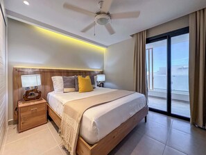 Ein modernes Hotelzimmer mit einem großen Bett, einem Holzkopfbrett, Nachttischen mit Lampen, einem Deckenventilator und Blick auf die Stadt durch große Fenster.