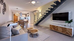 A modern living room with a sofa, a coffee table, a TV, and a staircase. - Gorgeous Penthouse with Rooftop and Ocean Views (Punta Cana)