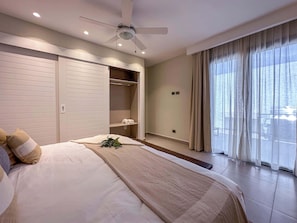 Ein Schlafzimmer mit einem Bett, Deckenventilator, einem Fenster mit Vorhängen und Blick auf das Wasser.