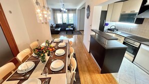 A modern kitchen with a central island, a dining area with a long table set for six, and a living area with a sofa and coffee table.
