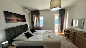 A modern bedroom with a large bed, a desk, and a view of the sea.