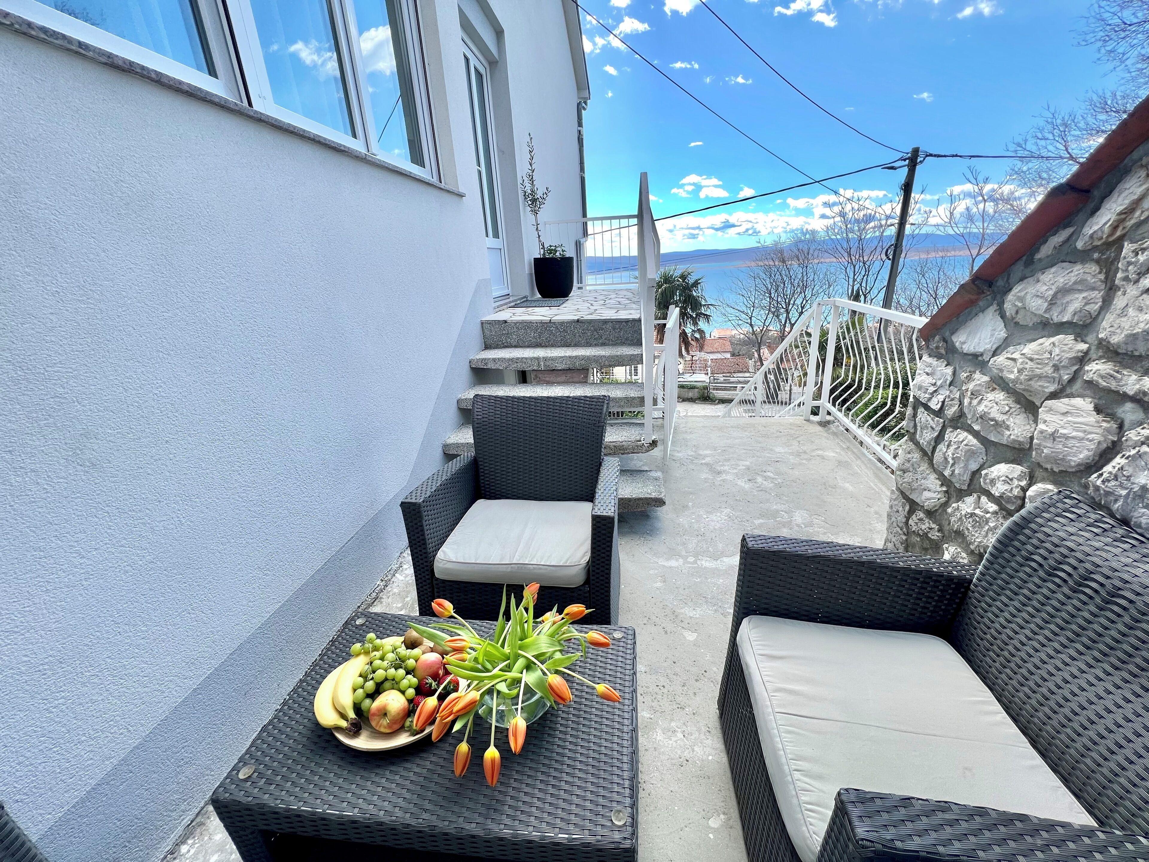 Een terras met rieten meubilair, een bloem- en fruitstuk, en een uitzicht op bergen.