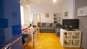 A modern living room with a sofa, a TV on a stand, a dining table with chairs, and a bookshelf. - Cozy 2BR Apartment near Piazza Navona (Roma)