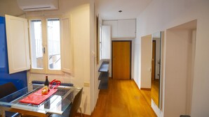 A narrow hallway with wooden flooring, a glass table with a red placemat and a bottle, and a door leading to a room with a wooden door. - Cozy 2BR Apartment near Piazza Navona (Roma)