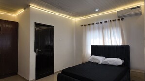 Ein Schlafzimmer mit einem schwarzen Bett, weißen Vorhängen, einer schwarzen Tür und LED-Leuchten entlang der Decke.