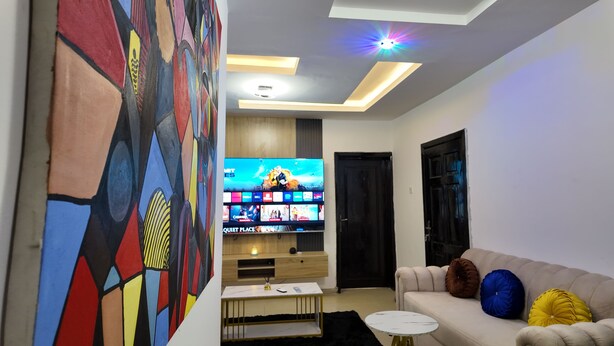 Ein modernes Wohnzimmer mit Flachbildfernseher, einer Couch mit Dekokissen, einem Couchtisch und einem farbenfrohen, abstrakten Gemälde an der Wand.