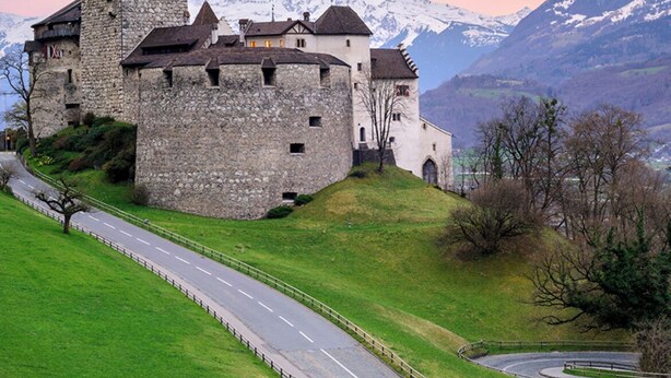 Un château de pierre historique, doté d’une tour imposante, situé sur une colline, avec une route menant à ses portes.