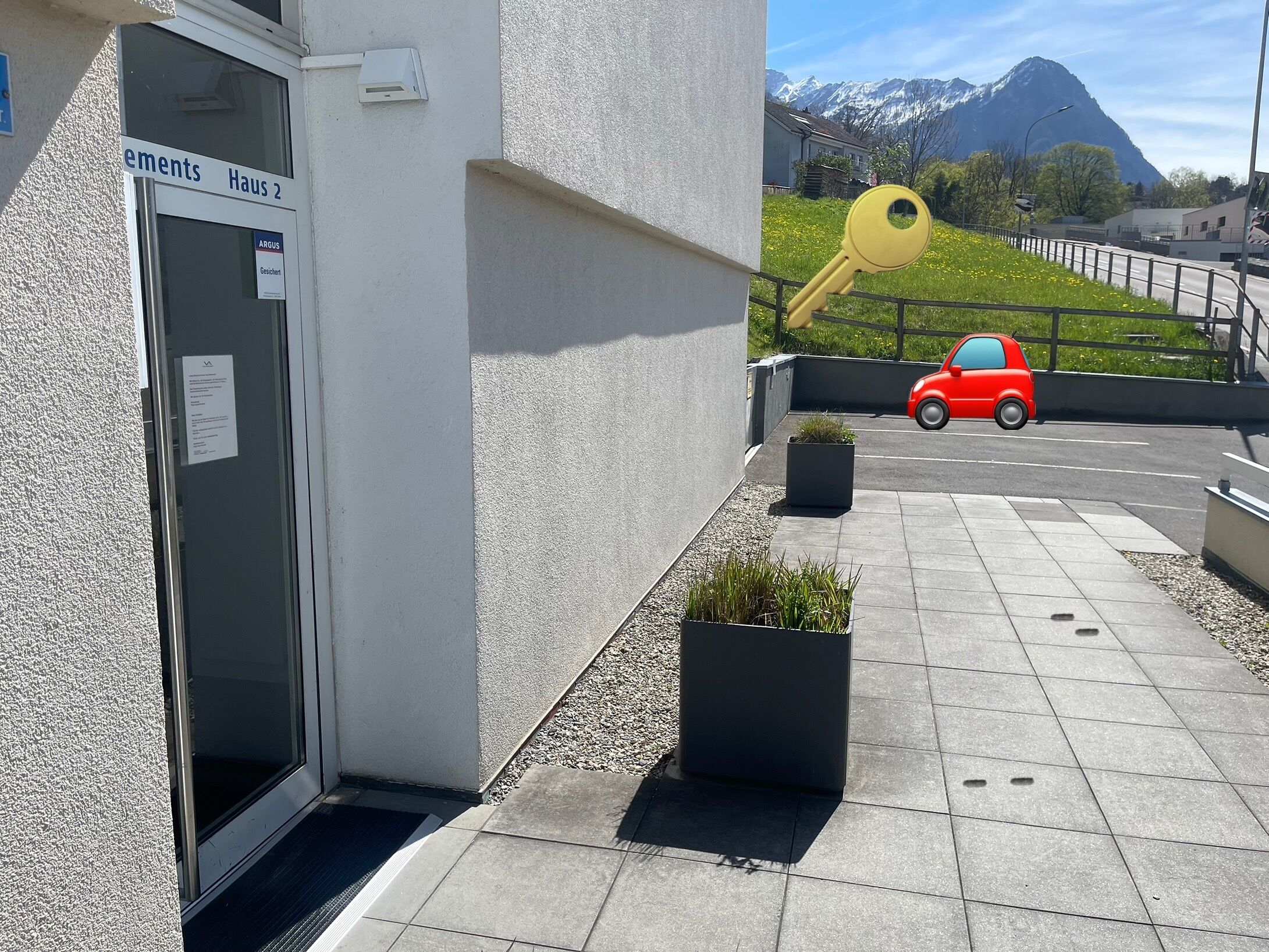 A building entrance with a sign, a red car parked outside, and a mountain in the background.