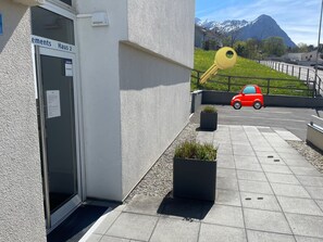 A building entrance with a sign, a red car parked outside, and a mountain in the background.