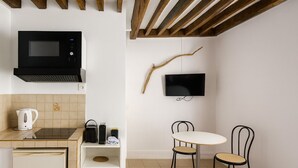 Eine kompakte Küche mit Mikrowelle, Wasserkocher und kleinem Kühlschrank. Es gibt eine Essecke mit Tisch und zwei Stühlen.