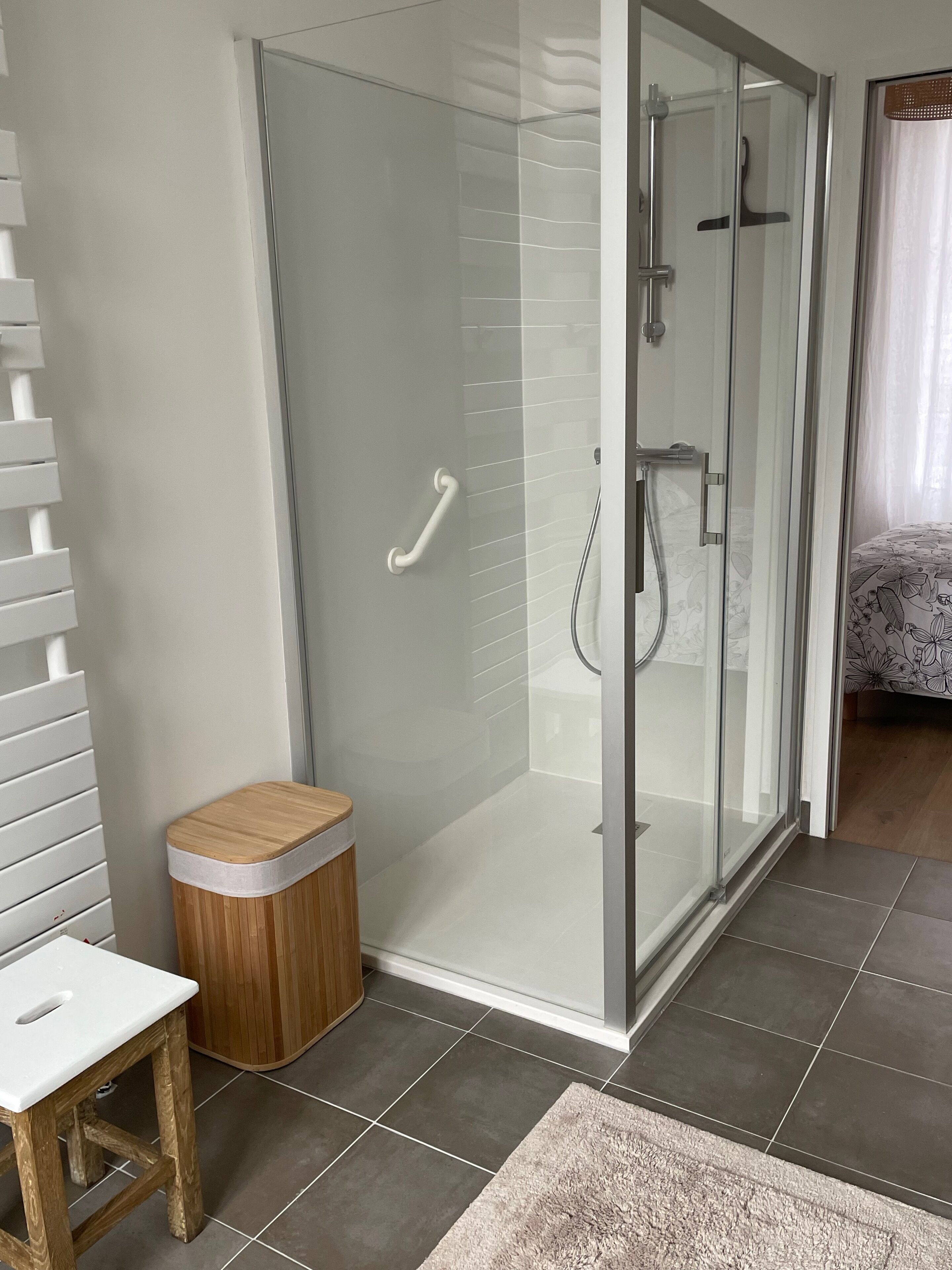 A modern bathroom with a glass shower enclosure, a wooden stool, and a white bench.