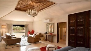 Ein geräumiges Zimmer mit einem großen Bett, zwei Sofas, einem Couchtisch und einem Essbereich. Ein großes Fenster sorgt für Tageslicht und bietet Blick ins Grüne.