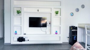 Un salon moderne avec un téléviseur à écran plat fixé à un mur blanc, entouré d’étagères intégrées et d’objets décoratifs.