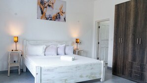 Une chambre à coucher avec un lit blanc, deux tables de chevet avec des lampes, une armoire en bois et un tableau au mur.