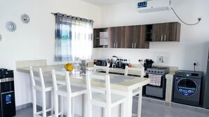 Une cuisine moderne avec des meubles blancs, un îlot central doté de chaises, un four encastré, une machine à café et un lave-linge.