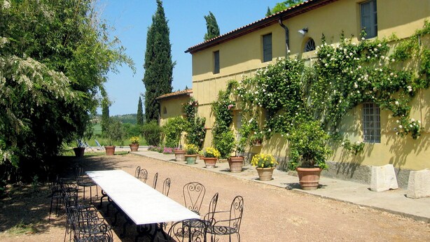 A courtyard with a long table and chairs, surrounded by potted plants and a building with a tiled roof. - Authentic Tuscan farmhouse with pool for families and children (Toscana)