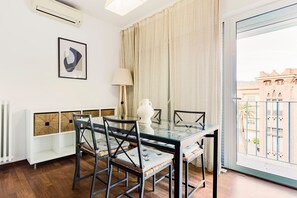 Enjoy meals at the glass dining table surrounded by comfortable chairs, with a view of the building's arched windows and balcony.