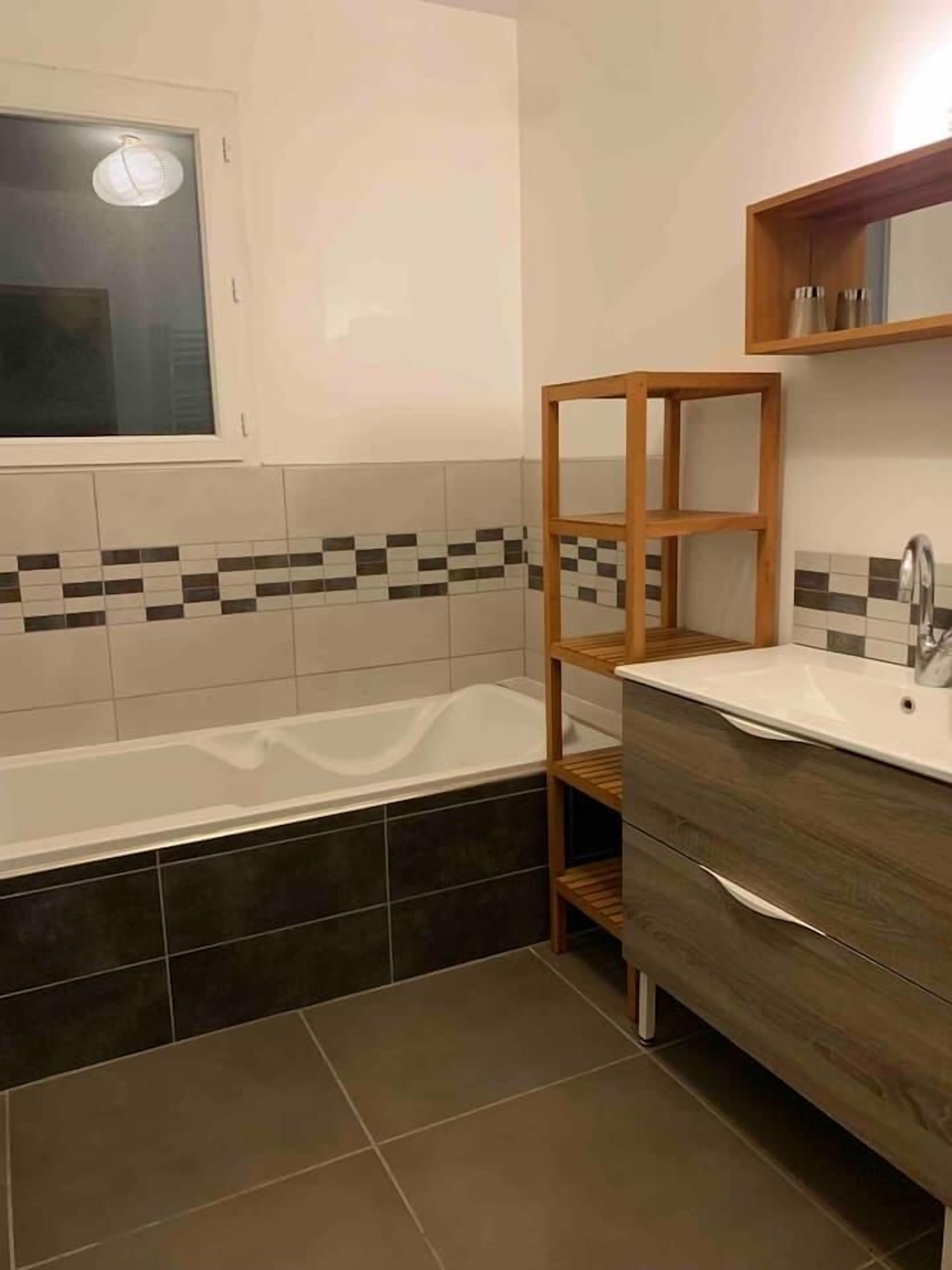 Ein modernes Badezimmer mit einer Badewanne, einem Holzregal und einem Waschtisch.