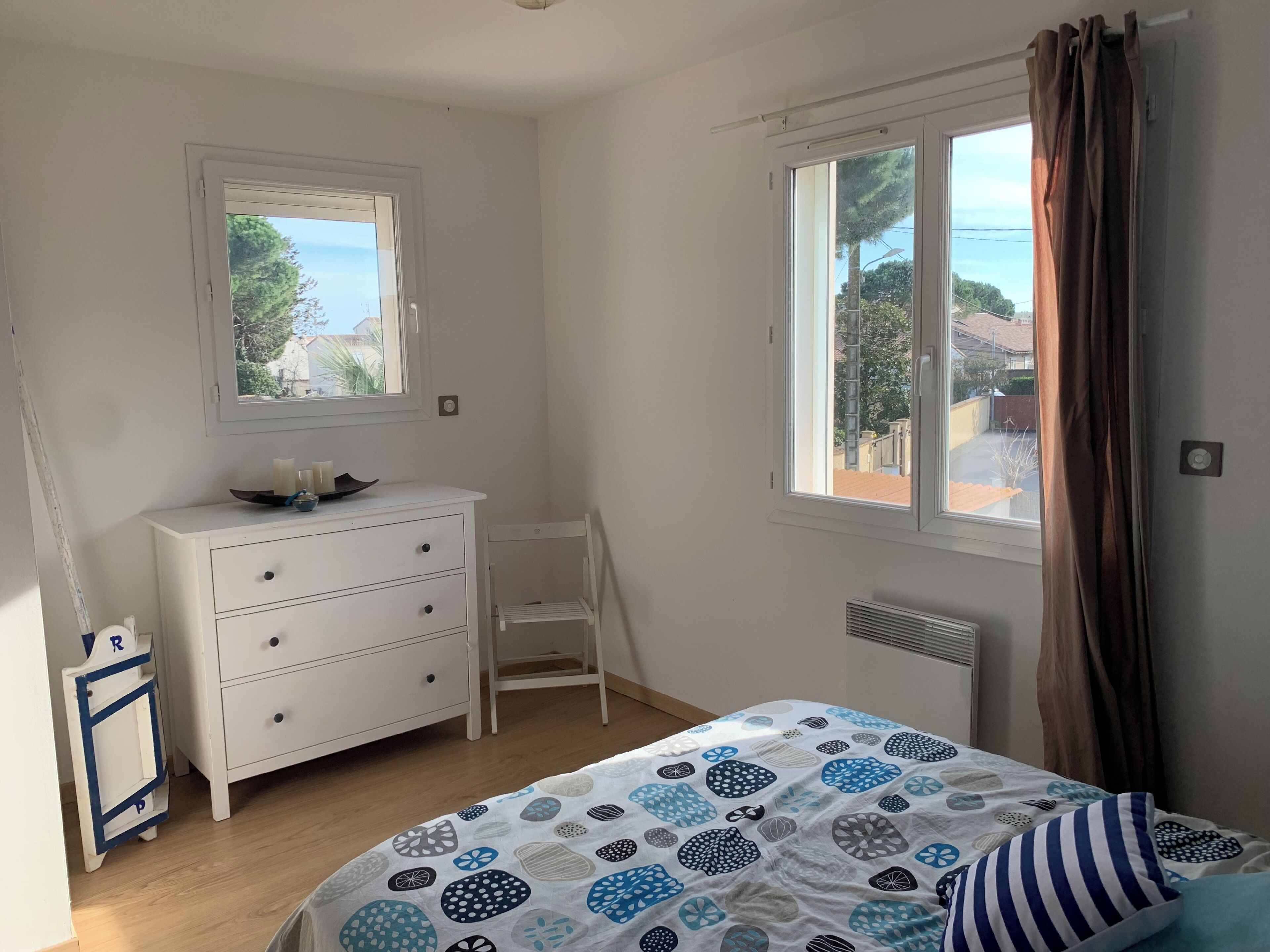 A bedroom with a bed, a dresser, a chair, and two windows.