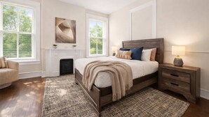 A bedroom with a large bed, a nightstand, a fireplace, and two windows with blinds. - Spacious brick home close to dining and nightlife! (Louisville)