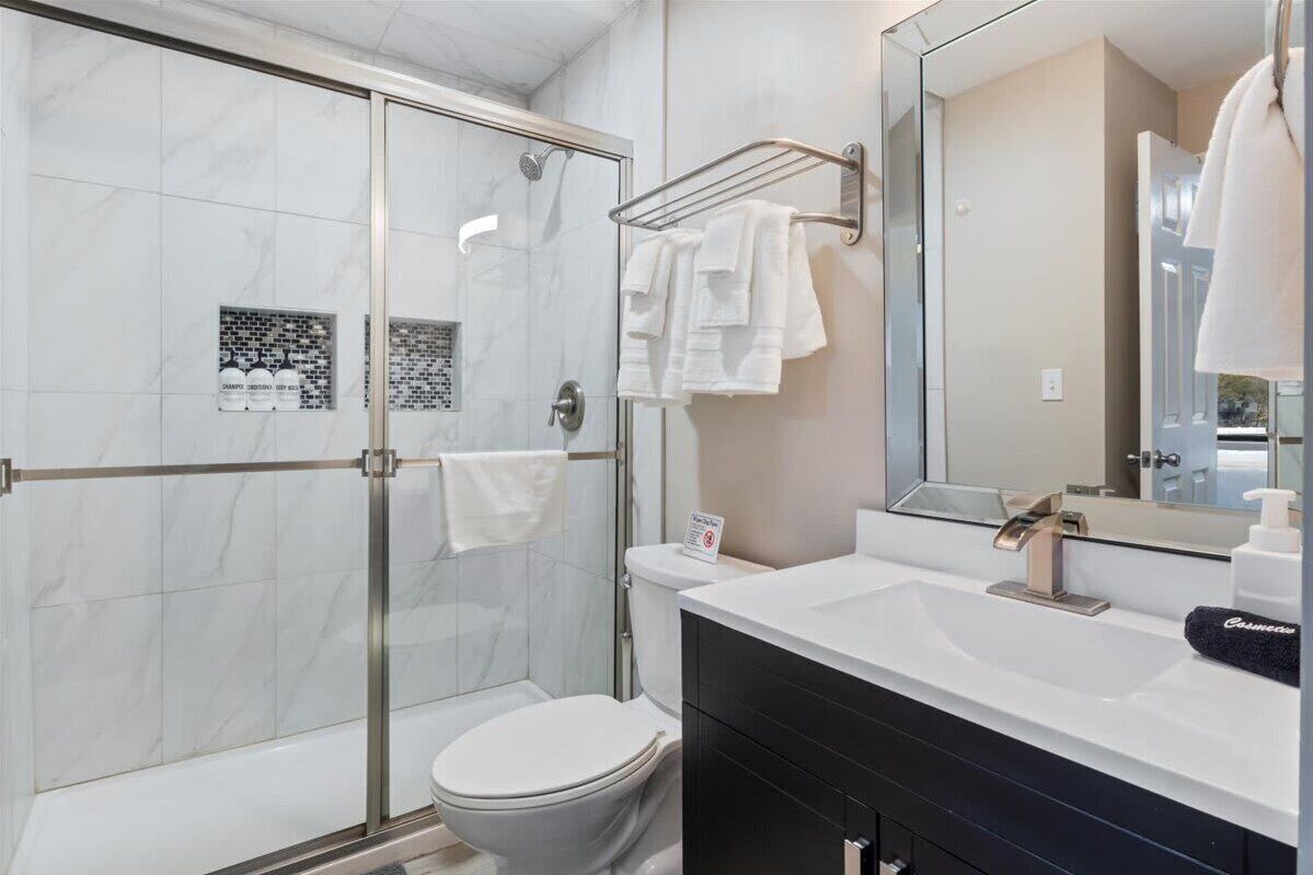 Ein modernes Badezimmer mit Duschkabine aus Glas, weißer Toilette, großem Spiegel und schwarzem Waschtisch.