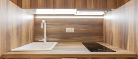 Una cocina moderna con un lavamanos empotrado, un grifo, una placa de inducción y armarios de madera.