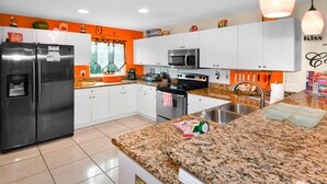A modern kitchen with white cabinets, a stainless steel refrigerator, a microwave, and a granite countertop.