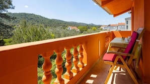 Un balcon donnant sur une colline, une table avec des chaises et une rambarde.