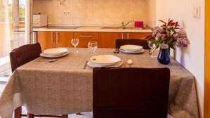 Un coin repas avec une table dressée pour deux personnes, des meubles en bois, un four à micro-ondes et un vase rempli de fleurs.