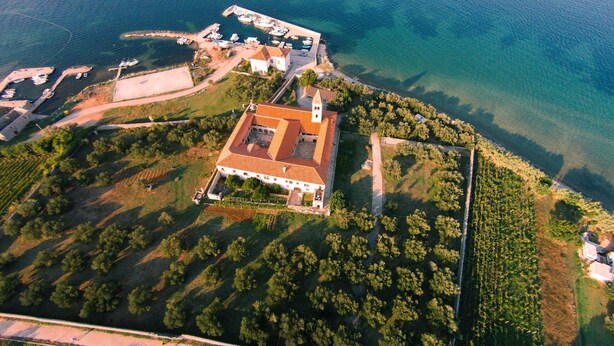 Vue aérienne d’une propriété située sur la côte, avec un bâtiment central, une marina avec des bateaux et une végétation luxuriante tout autour.