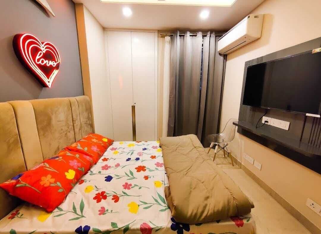 A bedroom with a bed, a TV, a neon heart sign, and a window with curtains.