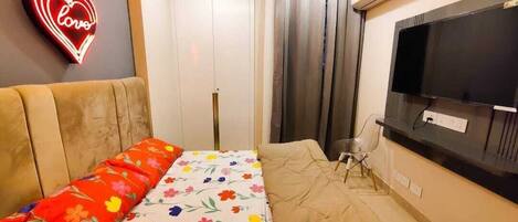 A bedroom with a bed, a TV, a neon heart sign, and a window with curtains.