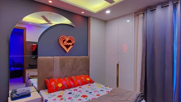 A bedroom with a bed, a nightstand, a ceiling fan, and a neon heart sign on the wall. - VINANDA (New Delhi)