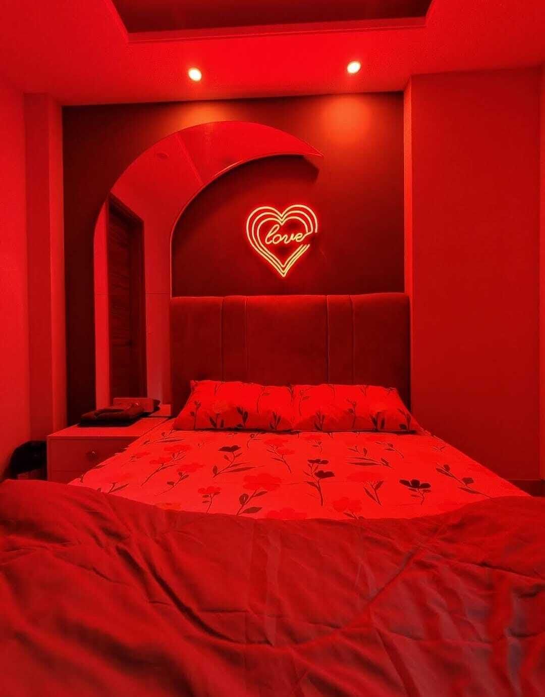 A red-themed bedroom with a neon heart-shaped sign that reads "love" on the wall.