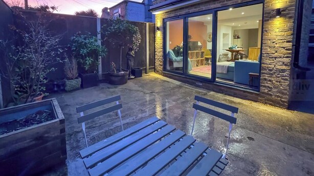A patio area with two wooden benches, a stone wall, and a glass door leading to a room with furniture inside. - Modern Margate Maisonette close to the beach by Adliv (Margate)
