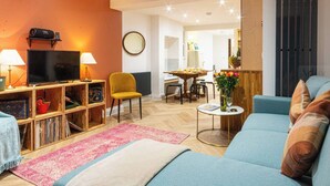 A living room with a TV, wooden shelving, a yellow chair, a blue sofa, and a dining area in the background. - Modern Margate Maisonette close to the beach by Adliv (Margate)