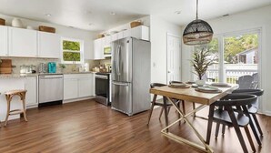 Une cuisine moderne avec des meubles blancs, des appareils en acier inoxydable et une table à manger en bois, assortie de chaises.