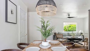 Un coin repas avec une table en bois dressée pour six personnes, entourée de sets de table en fibres tressées et agrémentée d’une plante en pot placée au centre.