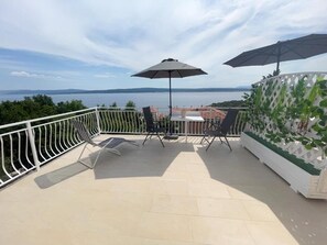 A balcony with a table and chairs, two umbrellas, and a view of the sea. - Apartman Florijan 1 (Crikvenica)
