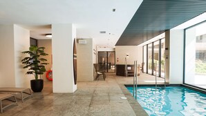 A modern indoor swimming pool area with a clear view of the pool, a potted plant, and a seating area with chairs. - Retreat in Providencia | Steps to Attractions (Providencia)