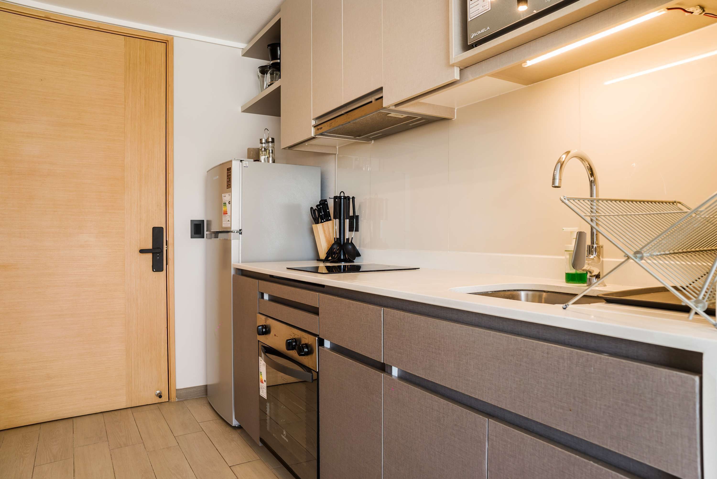 Een moderne keuken met een houten deur, roestvrijstalen apparatuur en een wit aanrecht.