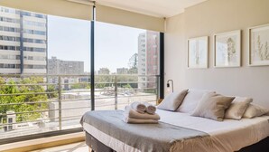A bedroom with a large window, a bed with pillows, and three framed pictures on the wall. - Perfect and Cozy Studio in Nunoa Ideal for 2 (Ñuñoa)