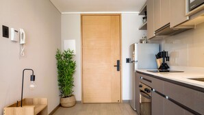 A modern kitchen with a wooden door, built-in appliances, and a potted plant. - Perfect and Cozy Studio in Nunoa Ideal for 2 (Ñuñoa)