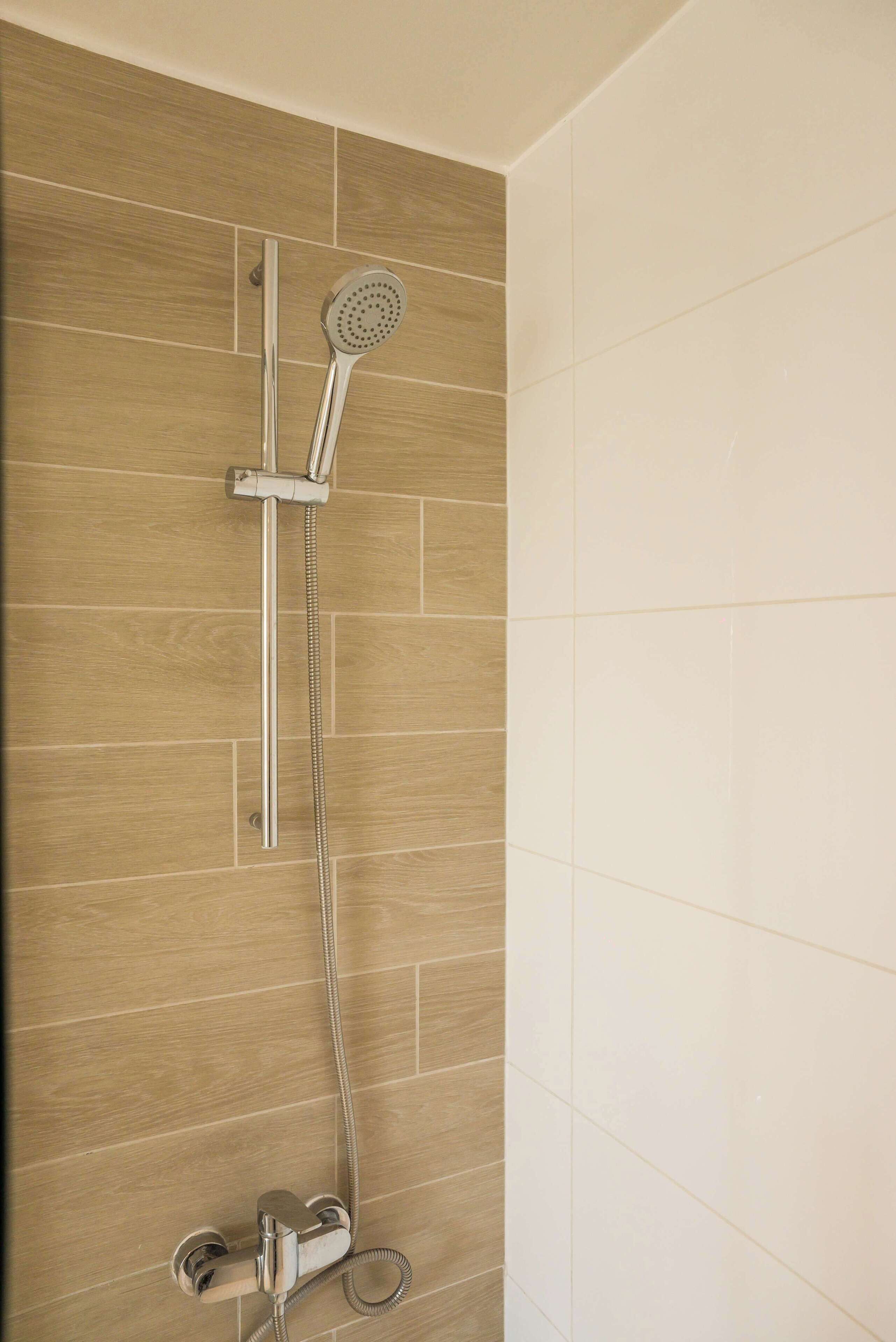 Une douche équipée d’un pommeau de douche à main et de commandes murales.