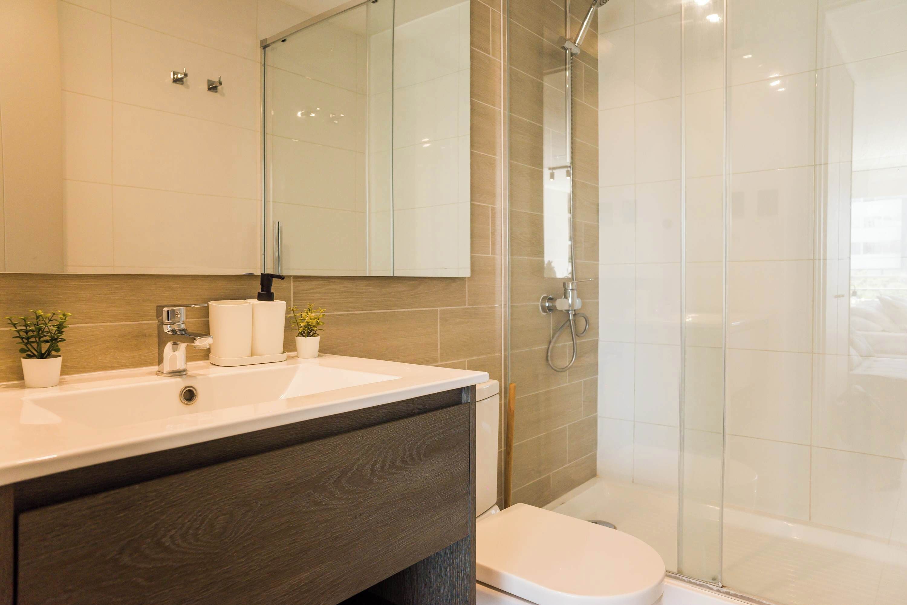 Une salle de bain moderne avec un lavabo blanc, un meuble-lavabo en bois foncé, des toilettes et une cabine de douche en verre.