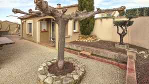Un arbre dont le tronc présente une structure particulière, situé dans un espace paysager avec une maison en arrière-plan.