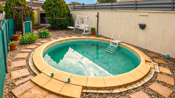 Une piscine ronde avec un escalier, entourée de chemins pavés de petits galets et de plantes en pot.