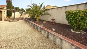 Une cour avec un sol de gravier, un petit muret en pierre et diverses plantes en pot.