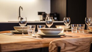 Mesa de jantar posta com vários copos de vinho e tigelas, com uma cozinha moderna ao fundo.