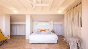 A spacious bedroom with a large bed, a ceiling fan, a macrame curtain, and a yellow chair.